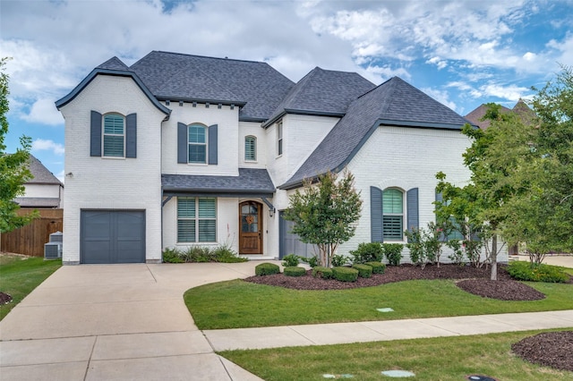 french country inspired facade with a front yard, a garage, and central air condition unit