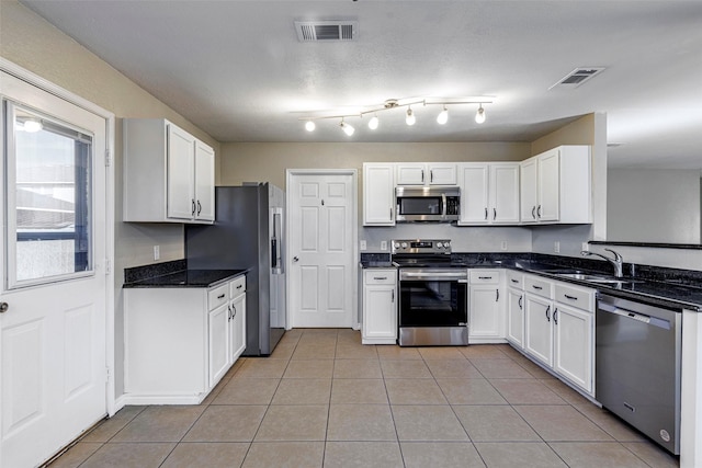 kitchen featuring appliances with stainless steel finishes, light tile patterned floors, dark stone counters, white cabinets, and sink