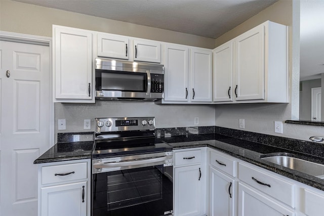 kitchen with a textured ceiling, white cabinets, dark stone counters, appliances with stainless steel finishes, and sink