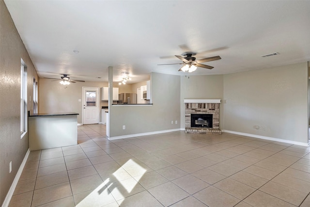 unfurnished living room with ceiling fan, a fireplace, and light tile patterned floors