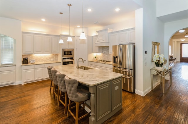 kitchen featuring stainless steel appliances, an island with sink, light stone counters, sink, and white cabinetry