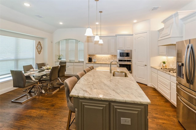 kitchen with decorative light fixtures, a kitchen bar, a kitchen island with sink, white cabinets, and appliances with stainless steel finishes