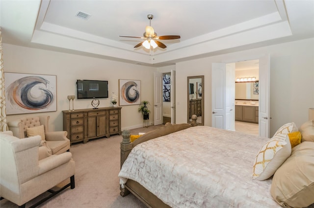 bedroom with ensuite bathroom, a raised ceiling, ceiling fan, and light carpet