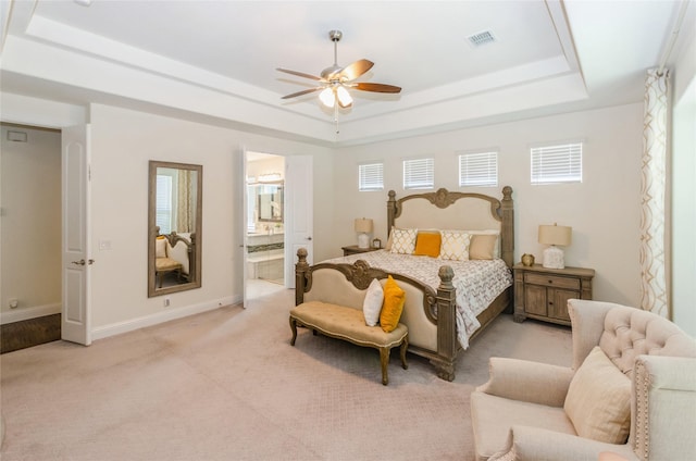 bedroom featuring ceiling fan, light colored carpet, ensuite bath, and a tray ceiling