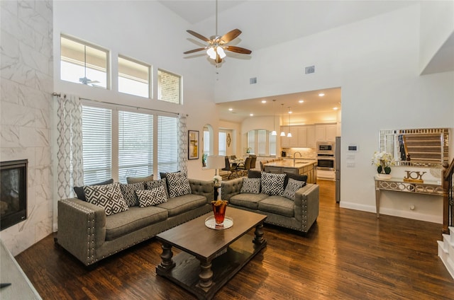 living room with a high ceiling, a premium fireplace, ceiling fan, and dark hardwood / wood-style floors