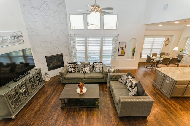 living room featuring a towering ceiling, a premium fireplace, ceiling fan, and dark hardwood / wood-style floors