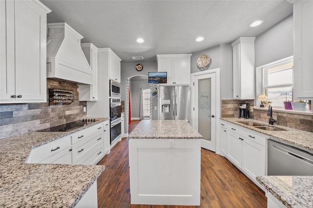 kitchen featuring custom range hood, white cabinetry, light stone counters, and appliances with stainless steel finishes