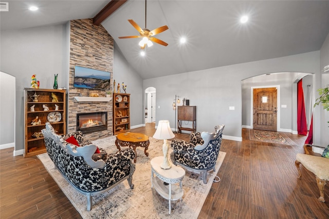 living room with high vaulted ceiling, beam ceiling, dark hardwood / wood-style flooring, ceiling fan, and a stone fireplace