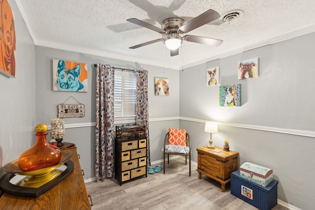 living area with a textured ceiling, ceiling fan, crown molding, and light wood-type flooring