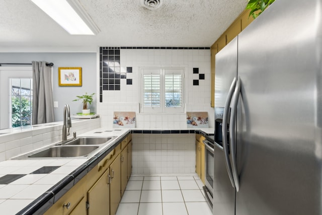 kitchen with sink, a textured ceiling, light tile patterned flooring, tile counters, and appliances with stainless steel finishes