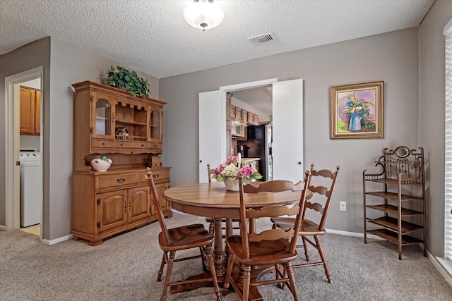 dining space with a textured ceiling, light colored carpet, and washer / dryer