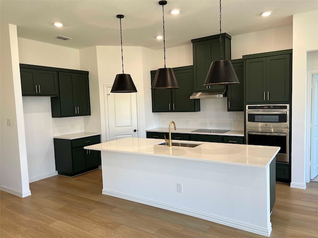 kitchen featuring an island with sink, pendant lighting, black electric cooktop, sink, and tasteful backsplash