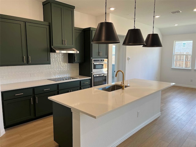 kitchen with double oven, a center island with sink, and decorative light fixtures