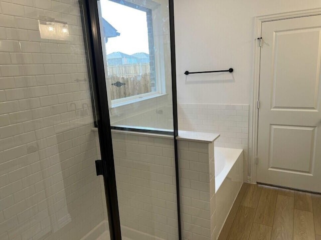 bathroom with tile walls, wood-type flooring, and independent shower and bath