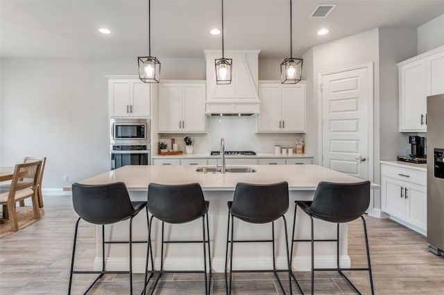 kitchen with a center island with sink, white cabinets, pendant lighting, and appliances with stainless steel finishes