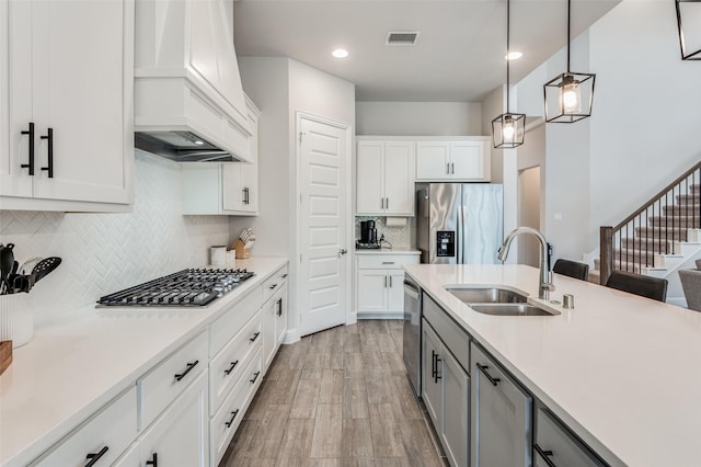 kitchen with sink, white cabinetry, hanging light fixtures, premium range hood, and appliances with stainless steel finishes