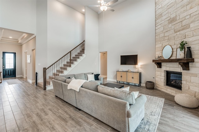 living room with a high ceiling, ceiling fan, crown molding, and a stone fireplace