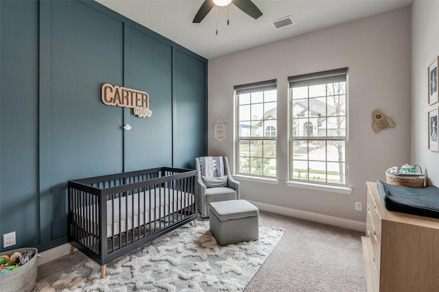 carpeted bedroom with ceiling fan and a crib