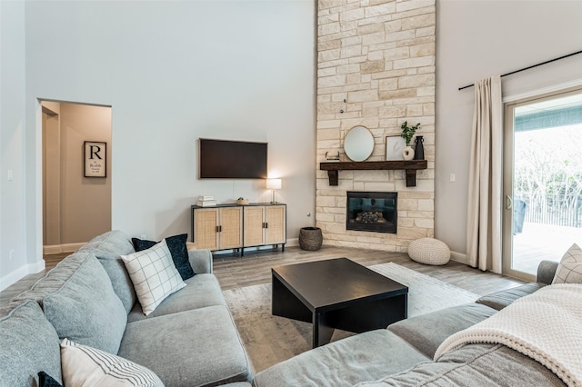 living room featuring a high ceiling, light wood-type flooring, and a stone fireplace