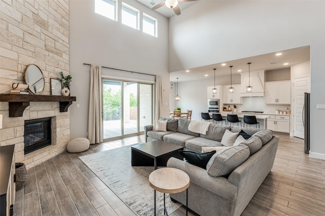 living room with a high ceiling, ceiling fan, and a stone fireplace