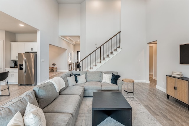 living room featuring ornamental molding, light wood-type flooring, and a towering ceiling