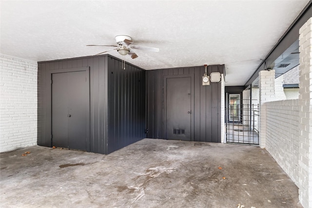 interior space featuring a textured ceiling, brick wall, wood walls, concrete floors, and ceiling fan