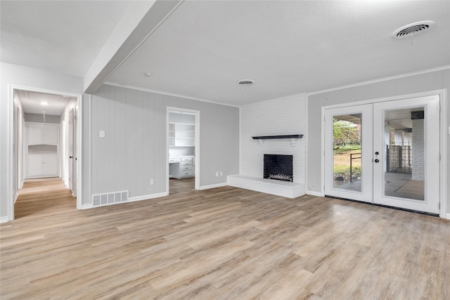 unfurnished living room featuring a fireplace, light wood-type flooring, built in features, and french doors