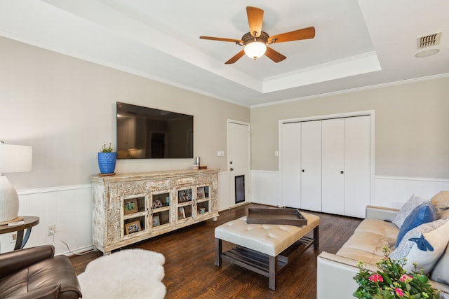 living room featuring ceiling fan, dark wood-type flooring, a tray ceiling, and ornamental molding