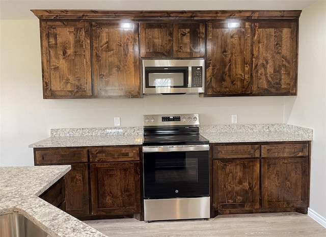 kitchen with dark brown cabinetry, appliances with stainless steel finishes, and light wood-type flooring