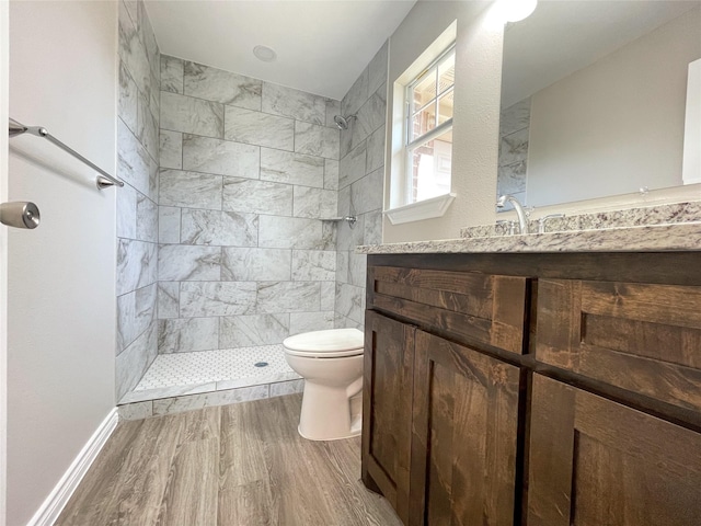 bathroom with vanity, toilet, wood finished floors, and a tile shower