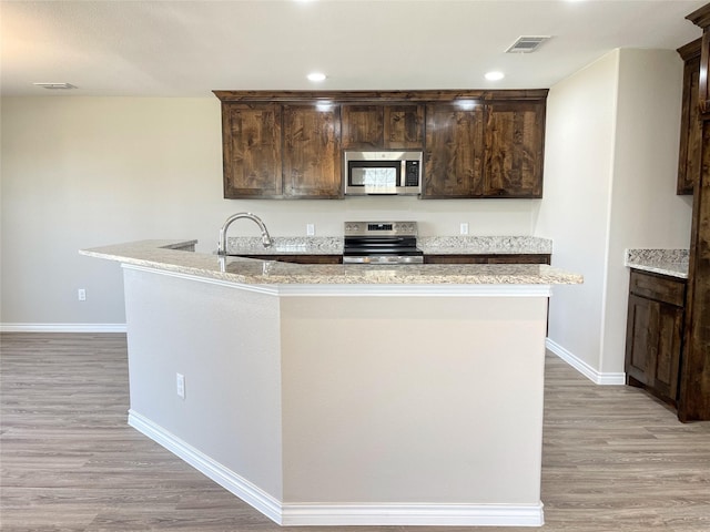 kitchen featuring visible vents, dark brown cabinets, light wood-type flooring, stainless steel appliances, and a sink