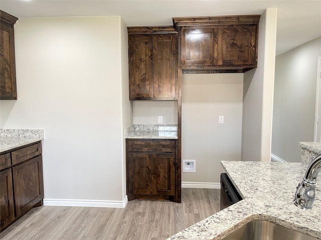 kitchen featuring baseboards, dark brown cabinetry, light wood-type flooring, light stone counters, and a sink