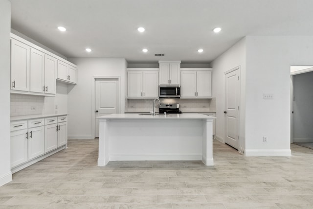 kitchen with stainless steel appliances, a kitchen island with sink, sink, and white cabinets