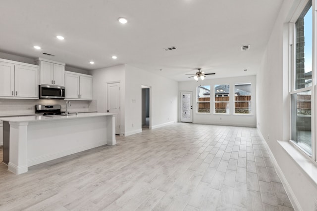 kitchen featuring an island with sink, white cabinets, backsplash, ceiling fan, and stainless steel appliances