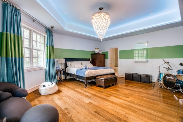 bedroom with ensuite bath, light wood-type flooring, a tray ceiling, and a chandelier