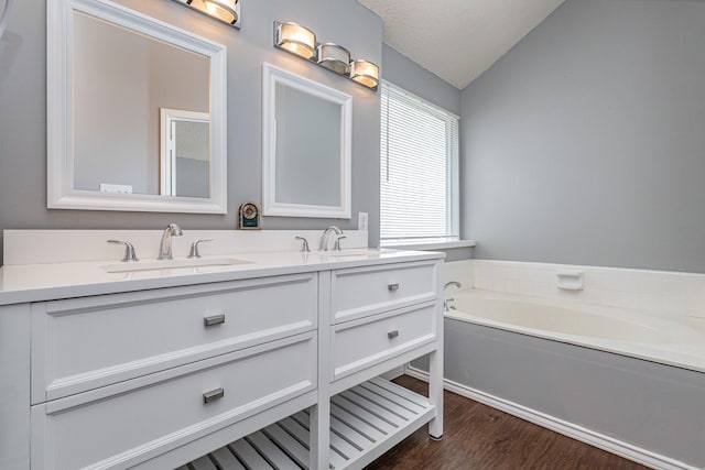 bathroom with a textured ceiling, vaulted ceiling, a bath, hardwood / wood-style flooring, and vanity