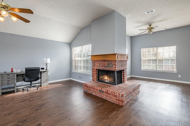 living room with a textured ceiling, vaulted ceiling, ceiling fan, a brick fireplace, and dark wood-type flooring