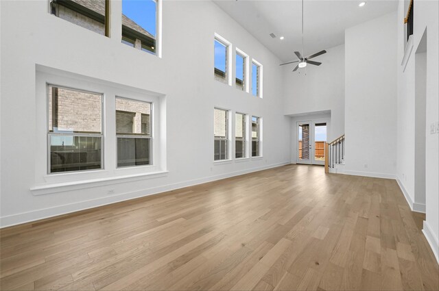 living room featuring a high ceiling, a fireplace, ceiling fan, and light hardwood / wood-style floors