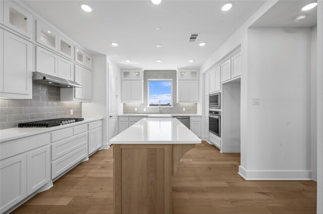 kitchen with appliances with stainless steel finishes, light wood-type flooring, white cabinets, decorative light fixtures, and sink