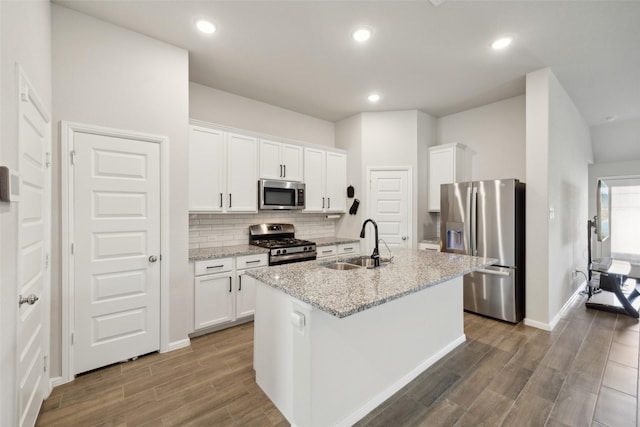 kitchen featuring a center island with sink, stainless steel appliances, light stone countertops, white cabinets, and sink