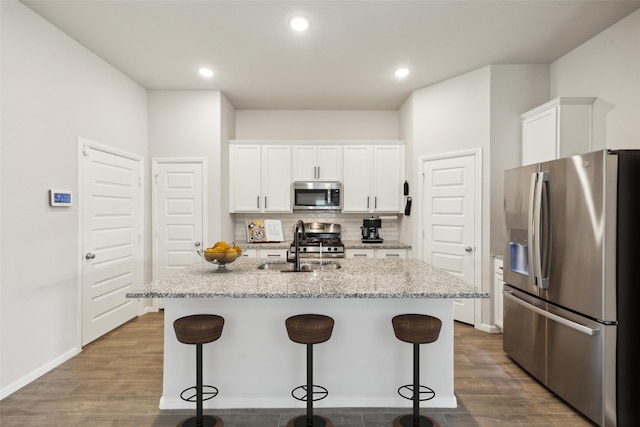 kitchen with light stone countertops, an island with sink, stainless steel appliances, and white cabinetry