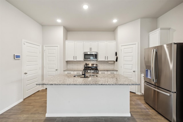 kitchen featuring dark wood-type flooring, white cabinetry, stainless steel appliances, decorative backsplash, and a kitchen island with sink