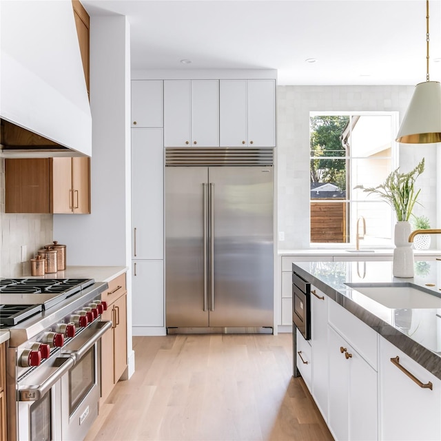 kitchen with premium appliances, custom exhaust hood, light stone counters, and white cabinetry