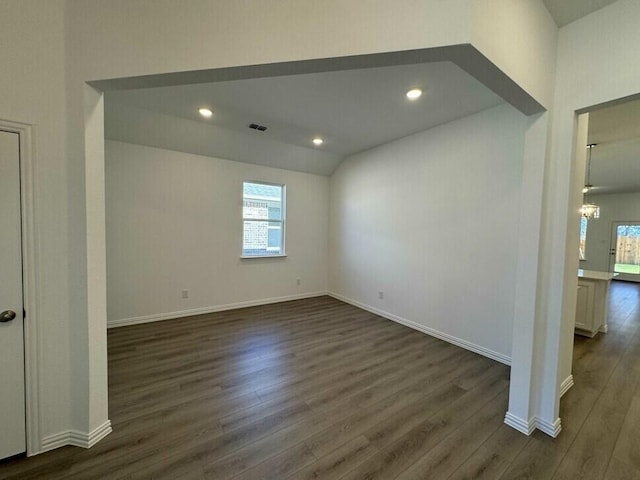 unfurnished room with a healthy amount of sunlight, dark hardwood / wood-style flooring, vaulted ceiling, and a chandelier