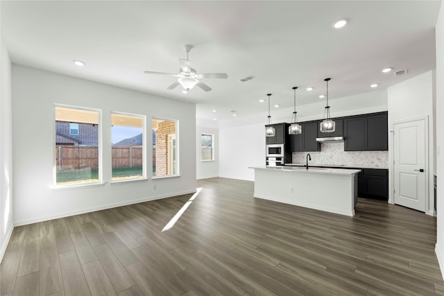 kitchen with an island with sink, ceiling fan, pendant lighting, decorative backsplash, and sink