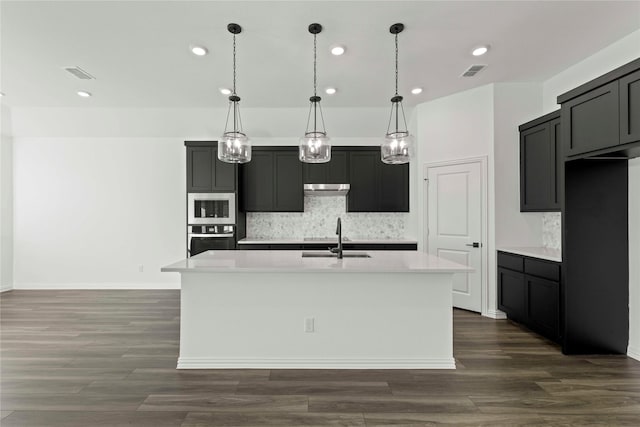 kitchen with a center island with sink, stainless steel appliances, pendant lighting, decorative backsplash, and sink