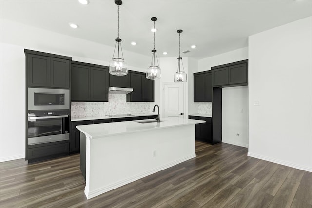 kitchen with stainless steel oven, pendant lighting, an island with sink, built in microwave, and sink