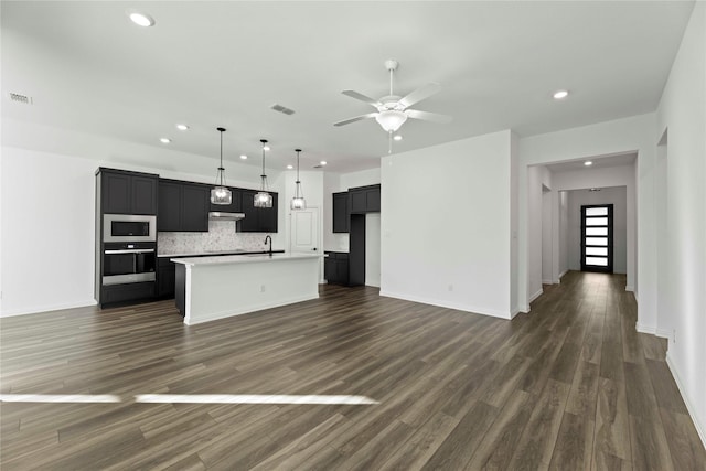 kitchen featuring stainless steel oven, an island with sink, built in microwave, and tasteful backsplash