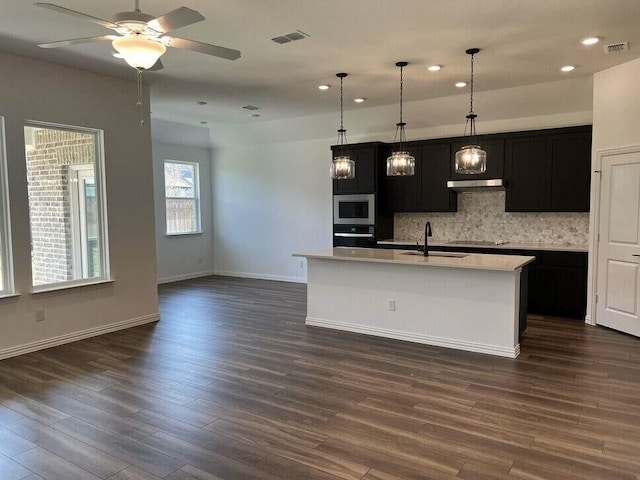 kitchen with hanging light fixtures, a center island with sink, wall oven, decorative backsplash, and sink