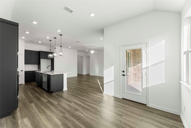 kitchen with sink, ceiling fan, backsplash, dark hardwood / wood-style floors, and a kitchen island with sink